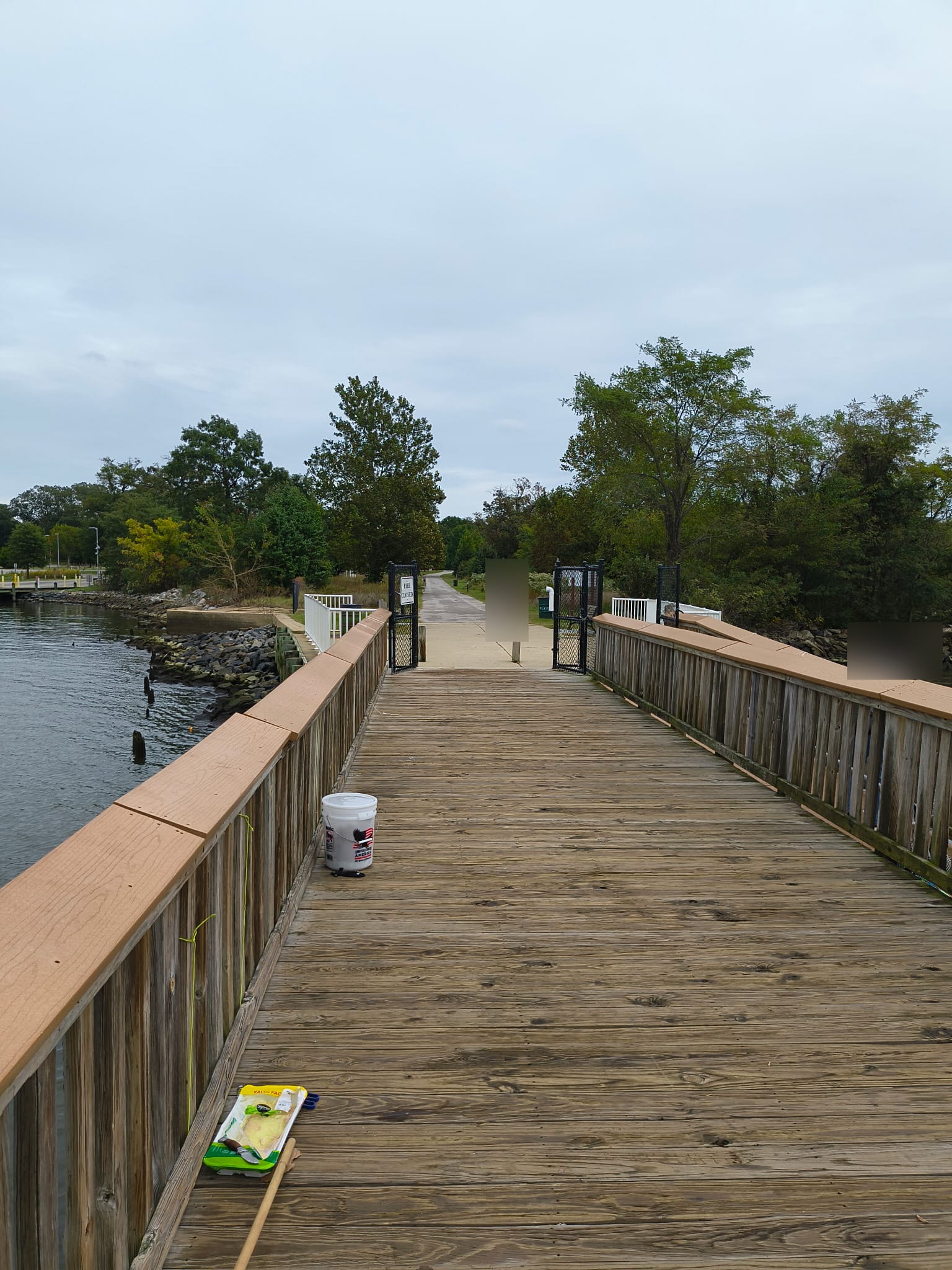 Looking back toward the park from the pier. A closure sign is visible beside the open gate; the owner separately confirmed that the pier was open. Visitors have been obscured.